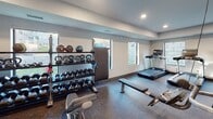 The fitness center at 2115 Marshall Ave in Saint Paul, Minnesota, is a thoughtfully designed, single-floor facility offering a comprehensive range of exercise equipment and functional workout zones. The space features durable speckled rubber flooring throughout, providing both safety and resilience underfoot, while recessed lighting illuminates the interior evenly across all areas.

The cardio section is equipped with treadmills, an elliptical trainer, a stationary bike, and a rowing machine, all arranged along a wall lined with multiple windows that allow natural light to filter in and provide views of the surrounding exterior. Adjacent to the cardio zone, a dedicated strength training area houses a multi-station cable machine by Life Fitness, a flat workout bench, and an adjustable free-weight bench with accompanying accessories.

A well-stocked free weights area features a full rack of dumbbells in graduated sizes, kettlebells, and medicine balls, organized neatly on tiered storage racks. Mirrored walls in the strength zone enhance spatial awareness during workouts. The facility also includes dual wall-mounted drinking fountains for convenient hydration access. A glass-panel partition and a separate entry door help define distinct workout zones within the open layout, contributing to an organized and functional overall environment.