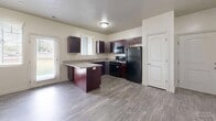 Located at 1475 N Main St in Layton, Utah, this single-floor unit offers a practical and comfortable layout across three bedrooms and two full bathrooms. The kitchen is a standout feature, boasting rich dark-wood cabinetry, granite-style countertops, wood-look plank flooring, and black appliances including a gas range, refrigerator, and dishwasher. A peninsula provides added counter space and a natural division between the kitchen and living areas, while a window over the sink invites natural light. The three bedrooms are finished with plush carpeting and feature windows fitted with blinds that allow for adjustable natural light and views of the surrounding area. The primary bedroom includes double closet doors, offering generous storage. Both bathrooms are finished consistently with wood-look flooring, dark vanity cabinetry, granite-style countertops, and full tub-shower combinations with clean white surrounds. A dedicated laundry room with side-by-side washer and dryer hookups and overhead shelving adds everyday convenience. The unit is connected by a hallway and maintains a cohesive, neutral color palette throughout, creating a clean and move-in-ready atmosphere.