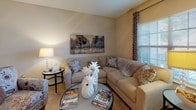 This single-floor residence offers a thoughtfully designed layout with a comfortable, cohesive aesthetic throughout. The living room serves as the heart of the home, featuring plush wall-to-wall carpeting, a ceiling fan with light fixture, and large windows with patio door access that flood the space with natural light. Neutral warm tones on the walls complement the room's welcoming ambiance.

Adjacent to the living area, a dedicated dining space accommodates a full dining table and seating, with a decorative mirror and console table adding an elegant touch. The galley-style kitchen is efficiently arranged with light wood cabinetry, white appliances including a full-size refrigerator and range, tile flooring, and ample counter space.

The primary bedroom is generously sized with carpet flooring, a ceiling fan, and access to an en-suite bathroom. A built-in vanity desk area with a window provides a functional workspace within the suite. The en-suite bath features a wide vanity with a large mirror. A second bedroom mirrors the comfort of the primary, with carpet flooring, multiple windows offering natural light, and a ceiling fan. A shared full bathroom with tile flooring, a wide vanity, and a large mirror serves the additional bedroom. Throughout the residence, consistent finishes and neutral tones create a harmonious and inviting environment.