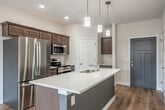 Located at 4185 Timothy Ct in De Forest, WI, this well-designed two-bedroom, two-bathroom residence offers a thoughtful single-floor layout with modern finishes throughout. The open-concept kitchen and living area serves as the heart of the home, featuring warm wood-toned cabinetry, a large central island with a quartz countertop and double sink, stainless steel appliances, and stylish pendant lighting overhead. Light hardwood flooring runs throughout the main living areas, enhancing the bright and airy atmosphere. Sliding glass doors open directly to a private balcony, allowing natural light to pour into the living space and providing pleasant outdoor views. A wall-mounted mini-split unit ensures year-round climate comfort, complemented by ceiling fans in both the living area and bedrooms. The primary bedroom is generously sized, offering plush carpeting, a ceiling fan, and direct access to its own en-suite bathroom and a spacious walk-in closet equipped with wire shelving. The bathrooms feature wood-toned vanities with white quartz countertops and hardwood-style flooring. A second well-proportioned bedroom and additional full bathroom with a shower round out the floor plan, with a second closet providing extra storage. Clean, neutral tones throughout give this residence a fresh and move-in-ready feel.