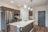 Located at 4185 Timothy Ct in De Forest, WI, this well-designed two-bedroom, two-bathroom residence offers a thoughtful single-floor layout with modern finishes throughout. The open-concept kitchen and living area serves as the heart of the home, featuring warm wood-toned cabinetry, a large central island with a quartz countertop and double sink, stainless steel appliances, and stylish pendant lighting overhead. Light hardwood flooring runs throughout the main living areas, enhancing the bright and airy atmosphere. Sliding glass doors open directly to a private balcony, allowing natural light to pour into the living space and providing pleasant outdoor views. A wall-mounted mini-split unit ensures year-round climate comfort, complemented by ceiling fans in both the living area and bedrooms. The primary bedroom is generously sized, offering plush carpeting, a ceiling fan, and direct access to its own en-suite bathroom and a spacious walk-in closet equipped with wire shelving. The bathrooms feature wood-toned vanities with white quartz countertops and hardwood-style flooring. A second well-proportioned bedroom and additional full bathroom with a shower round out the floor plan, with a second closet providing extra storage. Clean, neutral tones throughout give this residence a fresh and move-in-ready feel.