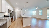 Located in Spring Hill, TN, this well-appointed 2-bedroom, 1-bathroom single-story home offers a thoughtfully designed open-concept layout with light wood-tone flooring throughout. The combined kitchen and living area serves as the heart of the home, anchored by a central island with granite countertops and an integrated sink illuminated by stylish pendant lighting. The kitchen is equipped with stainless steel appliances, including a refrigerator, electric range, and microwave, complemented by white shaker-style cabinetry and additional granite counter space along the perimeter. The spacious living area benefits from recessed lighting, a ceiling fan, and large windows that welcome ample natural light. Both bedrooms are generously proportioned, featuring light-filled windows with views of the surrounding greenery and the same consistent flooring found throughout the home. The full bathroom features a granite-topped vanity with shaker-style cabinetry, a large mirror, and a shower-tub combination. A dedicated laundry room houses a full-size Whirlpool washer and dryer with overhead shelving, adding everyday convenience. The home's clean, neutral palette and modern finishes create a bright and welcoming atmosphere throughout.