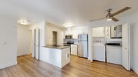 This well-appointed one-bedroom, two-bathroom unit offers a thoughtfully designed single-floor layout that maximizes every square foot. Light-toned wood-look flooring flows consistently throughout the space, lending a cohesive and modern aesthetic. The open-concept kitchen serves as the heart of the home, featuring white shaker cabinetry, a subway tile backsplash, dark countertops, and a full suite of stainless steel appliances including a refrigerator, electric range, and microwave. A peninsula with a built-in sink adds functional prep and casual dining space. A dedicated pantry with open shelving provides ample storage, while an in-unit washer is conveniently tucked just off the kitchen. The living area is bright and versatile, connecting seamlessly to the kitchen and hallway. The bedroom is a comfortable retreat, offering a window with green tree views, a baseboard heater, and access to a generously sized walk-in closet outfitted with multiple hanging rods and shelving. Two bathrooms serve the unit, one featuring a full soaking tub with a tiled surround and shower. Clean white walls, flush-mount lighting, and a neutral palette throughout give the space a fresh, move-in-ready feel.