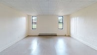 Located at Bedell Terrace in Hempstead, NY, this single-floor unit offers a straightforward, functional layout designed for comfortable everyday living. A long, clean hallway with tile flooring serves as the central spine of the unit, connecting each room with ease of access throughout.

The spacious main living area is a standout feature, offering generous proportions with large windows that allow natural light to pour in, providing views of the surrounding greenery. The room features tile flooring and a drop-panel ceiling, along with baseboard heating to ensure year-round comfort.

The kitchen is equipped with warm-toned wooden cabinetry — both upper and lower — a gas range, a refrigerator, and a double sink, providing a practical and efficient cooking space. Adjacent rooms include additional versatile spaces with carpeted flooring, drop-panel ceilings, and baseboard heating, suitable for use as bedrooms or flexible living areas. One room also features a closet for added storage.

The bathroom includes a full tub and shower combination with clean white tiling, chrome fixtures, and a window for natural ventilation. Throughout the unit, the neutral white walls and consistent finishes create a bright, cohesive atmosphere. Baseboard heating is present across multiple rooms, ensuring a consistently warm environment throughout the colder months.