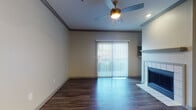 Located at 2811 La Frontera Blvd in Round Rock, Texas, this single-story unit offers a well-designed layout with a cohesive blend of modern finishes and comfortable living spaces throughout. The living area makes a strong impression with rich, dark hardwood-style flooring, crown molding, a ceiling fan, and a tile-surround fireplace that serves as a natural focal point. A sliding glass door floods the room with natural light and opens to a private balcony, providing a seamless connection to the outdoors. The kitchen is outfitted with dark cabinetry contrasted by light quartz-style countertops, a subway tile backsplash, and a full suite of stainless steel appliances including a range, over-the-range microwave, and refrigerator. A peninsula with an integrated sink adds both workspace and a casual dining option, while the open sightlines connect the kitchen to the main living area. The bedroom features plush carpeting, neutral walls, and a generously sized window that brings in abundant natural light. The bathroom is finished with dark vanity cabinetry, a white countertop, a well-lit mirror, and hardwood-style flooring that carries through from the hallway. Throughout the unit, consistent design choices and quality finishes create a polished, move-in-ready living environment.