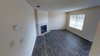 This two-floor residence offers a well-structured layout with a clean, functional design. The main living area is immediately notable for its rich, dark hardwood-style plank flooring, which extends throughout the space and adds warmth and visual depth. A corner fireplace serves as a standout architectural feature, framed by a classic white tile surround and hearth that anchors the room with a traditional yet timeless aesthetic. The walls are finished in a neutral, warm beige tone, creating a bright and versatile backdrop suitable for a variety of interior styles. A textured popcorn ceiling adds a layer of character consistent with the home's overall design. Natural light enters the living area through a window fitted with horizontal blinds, offering both illumination and privacy control. Overhead ventilation is provided via a ceiling-mounted HVAC register, ensuring climate comfort throughout. The open feel of the main level provides ample space for living and entertaining arrangements. With its combination of durable flooring, a functioning fireplace, and neutral finishes, this space offers a solid foundation that is move-in ready and easily adaptable to personal tastes across both floors.