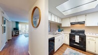 This single-floor residence offers a thoughtfully designed layout that balances comfort and functionality across its key living spaces. Warm hardwood-style flooring flows consistently throughout, lending a cohesive and inviting feel to every room.

The kitchen is a standout feature, equipped with white cabinetry, a double-basin sink, black appliances including an electric range and dishwasher, and a skylight overhead that fills the space with natural light. A circular wood-framed mirror accents the adjacent hallway entry, adding a decorative touch.

The open-concept living and dining area is generously proportioned, with warm-toned walls and a textured ceiling. The dining space benefits from a pendant light fixture and a built-in display niche, while large sliding glass doors in the living area provide views to the outdoors and allow ample natural light.

Two well-sized bedrooms each feature hardwood-style flooring, closet storage, and windows with outdoor views. The primary bedroom includes a dedicated closet and private en-suite bathroom access. Both bathrooms are outfitted with a tub-shower combination and tile surround, offering clean and functional designs.

The dollhouse view confirms a practical, efficient floor plan with well-connected rooms, making this a comfortable and versatile living space.