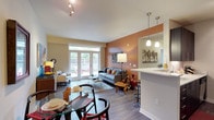 This single-floor residence offers a well-balanced open-concept layout that seamlessly connects the living, dining, and kitchen areas. The living room is a standout space, anchored by a warm terracotta accent wall, wood-look flooring, and French doors that open directly to a private outdoor patio, filling the room with natural light. A peninsula counter with pendant lighting defines the transition to the kitchen, which features dark espresso cabinetry, white countertops, a subway tile backsplash, and stainless steel appliances arranged in a practical galley configuration. The dining area complements the open layout with easy access to both the kitchen and living spaces. The primary bedroom is highlighted by a bold teal accent wall and direct access to a private bathroom equipped with a dark-cabineted vanity, a large mirror with bright vanity lighting, and a clean white shower enclosure. Additional bedrooms offer carpeted flooring, ample natural light through large windows, and generous closet space. A secondary bedroom provides its own exterior door access. Throughout the residence, a consistent palette of neutral tones, modern fixtures, and quality finishes creates a cohesive and inviting atmosphere suited for comfortable everyday living.