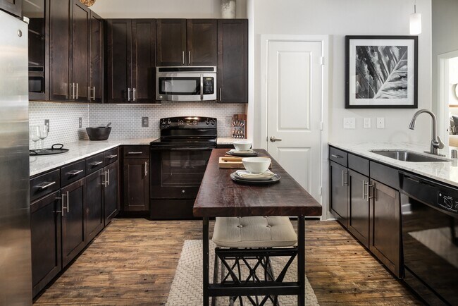 Cocina con gabinetes color espresso, encimeras de granito, protector contra salpicaduras de azulejos y pisos de tablones de vinilo de superficie dura. - Avalon Lakeside