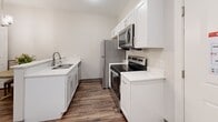 Located at 2917 Cozy Court in Evansville, Indiana, this single-story unit offers a well-organized layout across four functional spaces, designed with a clean, modern aesthetic. Warm-toned wood-look flooring runs consistently throughout, creating a cohesive and inviting atmosphere from room to room.

The kitchen is thoughtfully equipped with white shaker-style cabinetry, light quartz countertops, and a full suite of stainless steel appliances, including a refrigerator, electric range, and over-the-range microwave. A peninsula with a breakfast bar provides additional counter space and connects the kitchen to the living area, which offers a comfortable and straightforward setting with neutral walls and ample room for seating.

The bedroom features recessed lighting, a window fitted with blinds that allows natural light to filter in, and a private entry door, contributing to a sense of independence and functionality. A second, equally serene sleeping space includes a window with natural light and clean, neutral finishes.

The bathroom is designed with accessibility in mind, featuring stainless steel grab bars near the toilet and within the walk-in shower stall. Neutral walls and the consistent wood-look flooring maintain the unit's unified design language throughout.