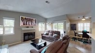 This single-floor home offers a thoughtfully designed layout with a variety of comfortable and functional spaces throughout. The living room serves as the heart of the home, featuring vaulted ceilings that lend a sense of openness and volume. A tiled fireplace with a clean white mantel anchors the room, flanked by multiple windows that invite an abundance of natural light. The space is further enhanced by stylish pendant lighting and views of lush greenery outdoors.

The galley-style kitchen is outfitted with rich, dark wood cabinetry, light countertops, a tile backsplash, and hardwood-style flooring. It connects seamlessly to the dining area, which features a ceiling fan, hardwood-style floors, and a bright window with shutters — an ideal space for everyday meals or entertaining.

The primary bedroom is generously sized with plush carpet and direct access to an en-suite bathroom. The en-suite features a vanity with a white countertop, modern fixtures, and a shower/tub combination. A second full bathroom offers similar finishes with a clean, neutral palette. An additional room with wide sliding closet doors and carpeted flooring provides flexibility as a bedroom or versatile bonus space. Throughout, the home maintains a cohesive gray tone with warm accents and practical finishes.