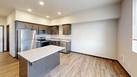 Located at 102 E Division St in Arlington, Washington, this efficiently designed single-floor unit makes excellent use of its compact footprint. The open layout seamlessly connects the living and kitchen areas, creating a functional and cohesive living space.

The kitchen is a standout feature, outfitted with rich dark-stained wood cabinetry extending to the ceiling for ample storage, light stone-look countertops, a tasteful tile backsplash, and a full suite of stainless steel appliances including a refrigerator, range, microwave, and dishwasher. A central island with a white quartz-style surface provides additional workspace and casual seating. Recessed lighting illuminates the space cleanly overhead.

The living area is bright and open, with neutral white walls, recessed lighting, and light wood-look luxury vinyl plank flooring that runs consistently throughout the unit, lending warmth and visual continuity.

The bathroom is notably spacious for the unit's overall size, featuring dark wood cabinetry with a long vanity and white countertop, a large mirror, and a stacked washer and dryer conveniently located within the same room — a practical and space-conscious design choice. Clean white walls and the same LVP flooring maintain a cohesive aesthetic. The unit also includes a set of double panel doors, adding a polished, finished touch to the interior.
