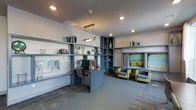 This single-floor space is a thoughtfully designed business center that balances functionality with contemporary style. The room is anchored by a custom built-in shelving system finished in a cool slate blue, which spans the walls and provides both storage and display space for decorative accents, books, and artwork. A dedicated workstation is integrated into the shelving unit, complete with a desktop computer, offering a focused area for individual work tasks.

Recessed ceiling lighting, complemented by a sleek pendant light fixture, provides ample illumination throughout the space. The neutral walls serve as a clean backdrop that allows the blue cabinetry and pops of color from the yellow-green upholstered armchairs to stand out. These chairs, paired near a framed art piece, create a comfortable lounge and conversation area ideal for informal meetings or relaxed reading.

The flooring features patterned carpet tiles that add texture and visual interest while maintaining a professional atmosphere. The overall ambiance is modern and inviting, with a cohesive color palette of blues, grays, and warm accent tones. This space is well-suited for residents or occupants seeking a productive yet comfortable environment for work or study.