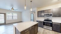 Located in Colorado Springs, CO, this well-appointed 2-bedroom, 2-bathroom single-floor residence offers a thoughtfully designed layout with contemporary finishes throughout. The open-concept kitchen and living area serves as the heart of the home, featuring dark espresso cabinetry with brushed nickel hardware, a white quartz-topped center island with pendant lighting, and a full suite of stainless steel appliances including a range, microwave, refrigerator, and dishwasher. Light wood-style flooring flows throughout the main living areas, complementing the neutral color palette. The living room is anchored by a sleek, modern linear fireplace with a white surround, adding warmth and style to the space. A glass-panel exterior door and large windows invite abundant natural light and outdoor views. Both bedrooms are carpeted and equipped with ceiling fans, with windows framing views of the surrounding landscape. The primary bedroom includes a spacious walk-in closet with built-in wire shelving for ample storage. The bathrooms are finished with wood-tone vanities, white quartz countertops, and light wood-look flooring, with a tub-shower combination in each. A hallway connects all rooms efficiently, completing this clean and functional floor plan.