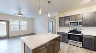 Located in Colorado Springs, CO, this well-appointed 2-bedroom, 2-bathroom single-floor residence offers a thoughtfully designed layout with contemporary finishes throughout. The open-concept kitchen and living area serves as the heart of the home, featuring dark espresso cabinetry with brushed nickel hardware, a white quartz-topped center island with pendant lighting, and a full suite of stainless steel appliances including a range, microwave, refrigerator, and dishwasher. Light wood-style flooring flows throughout the main living areas, complementing the neutral color palette. The living room is anchored by a sleek, modern linear fireplace with a white surround, adding warmth and style to the space. A glass-panel exterior door and large windows invite abundant natural light and outdoor views. Both bedrooms are carpeted and equipped with ceiling fans, with windows framing views of the surrounding landscape. The primary bedroom includes a spacious walk-in closet with built-in wire shelving for ample storage. The bathrooms are finished with wood-tone vanities, white quartz countertops, and light wood-look flooring, with a tub-shower combination in each. A hallway connects all rooms efficiently, completing this clean and functional floor plan.