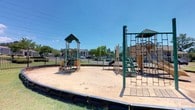 Located at 200 Colony Park Drive in Pearl, Mississippi, this outdoor recreational space is a well-equipped playground designed to serve the surrounding community. The area features multiple freestanding play structures with green-accented rooftops, offering a variety of engaging activities for children of different ages and skill levels. Among the standout elements are climbing ladders, chain-link climbing nets, and elevated platforms that encourage physical activity and coordination. The play structures are arranged across a generous sand-covered surface, which provides a safe and cushioned ground cover throughout the play area. A sturdy black perimeter border contains the sand and defines the boundaries of the playground. The entire space is enclosed by a black metal fence, offering a secure environment for children at play. Mature trees line the perimeter, providing some natural shade, while the open layout allows for ample sunlight throughout the day. The playground benefits from clear sightlines, making it easy for caregivers to supervise children from multiple vantage points. The surrounding landscape is well-maintained, contributing to the inviting and functional character of this community recreational facility.