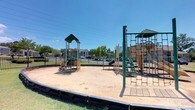 Located at 200 Colony Park Drive in Pearl, Mississippi, this outdoor recreational space is a well-equipped playground designed to serve the surrounding community. The area features multiple freestanding play structures with green-accented rooftops, offering a variety of engaging activities for children of different ages and skill levels. Among the standout elements are climbing ladders, chain-link climbing nets, and elevated platforms that encourage physical activity and coordination. The play structures are arranged across a generous sand-covered surface, which provides a safe and cushioned ground cover throughout the play area. A sturdy black perimeter border contains the sand and defines the boundaries of the playground. The entire space is enclosed by a black metal fence, offering a secure environment for children at play. Mature trees line the perimeter, providing some natural shade, while the open layout allows for ample sunlight throughout the day. The playground benefits from clear sightlines, making it easy for caregivers to supervise children from multiple vantage points. The surrounding landscape is well-maintained, contributing to the inviting and functional character of this community recreational facility.