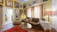 Located at 705 E Lindsay St in Stockton, CA, this single-floor, one-bedroom, one-bathroom home offers a compact yet thoughtfully arranged layout full of character and personality. The living room immediately captures attention with its warm yellow walls adorned floor-to-ceiling with an eclectic gallery of framed artwork, hardwood flooring, large draped windows that invite natural light, and a distinctive media console that anchors the space. The combined dining room and kitchen area transitions seamlessly from the living space, featuring tile flooring, warm wood cabinetry, a mosaic tile backsplash, light stone countertops, a stainless steel sink, and a window above that brightens the workspace. The dining area accommodates a round table beneath natural light from a curtained window, also decorated with an array of framed artwork. The bedroom offers a cozy retreat with plush carpeting, ornate crown molding, multiple windows with draping curtains, and a spacious walk-in closet. The bathroom is neatly appointed with a white vanity, tile flooring, and a tub-shower combination. A connecting hallway and dedicated closet complete the efficient floor plan of this uniquely expressive home.
