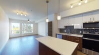 This single-floor unit at 5321 N Interstate Ave in Portland's Interstate corridor offers a thoughtfully designed open-concept layout finished with contemporary details throughout. Wide-plank hardwood-style flooring flows continuously from the kitchen through the living area, creating a cohesive and expansive feel.

The kitchen is a standout feature, showcasing a striking geometric-patterned tile backsplash in navy and white, a combination of white upper cabinetry and rich walnut-toned lower cabinets, and a full suite of stainless steel appliances including a refrigerator, range, microwave, and dishwasher. A large island with a clean white countertop provides additional workspace and casual seating. Pendant lighting and track fixtures illuminate the space with both style and function.

The open living area receives abundant natural light through a generously sized window framing views of mature trees, and is equipped with a ceiling fan. A barn-style sliding door adds an architectural accent near the entryway. The bedroom is bright and airy, with its own large window and ceiling fan.

The bathroom features marble-look tile flooring, a full tub-shower combination with large-format white tile surround, and warm wood-toned cabinetry with clean white countertops, completing the unit's modern aesthetic.