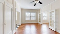 Located at 5272 Washington Pl in St. Louis's Central West End neighborhood, this single-floor apartment showcases a blend of classic architectural character and practical layout. Throughout the living areas, warm hardwood flooring runs consistently underfoot, complemented by crisp white millwork, detailed panel molding on the walls, and tall baseboards that reflect the building's heritage craftsmanship. Ceiling fans are present in the main rooms, and multiple windows fitted with blinds allow natural light to filter through, creating a bright and airy atmosphere.

The living and bedroom spaces feature generously proportioned rooms with notable ceiling height, panel-trimmed walls, and elegant double doors with transom-style detailing that add a sense of architectural refinement. A pair of French doors connects rooms, enhancing the open flow of the interior. Closet storage is integrated with paneled double doors that maintain the cohesive aesthetic.

The kitchen is a standout space, featuring a striking black-and-white checkered tile floor that contrasts boldly with white cabinetry, countertops, and white appliances including a refrigerator and electric range. The galley-style layout makes efficient use of the space.

The bathroom maintains the unit's clean, neutral palette with white fixtures, a built-in shelf with mirror, and classic chrome hardware, providing a functional and tidy finish to the overall space.