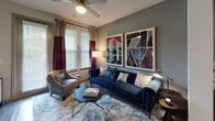 This thoughtfully designed single-floor residence offers a cohesive blend of contemporary style and everyday functionality. The kitchen is a standout feature, equipped with stainless steel appliances including a refrigerator, dishwasher, built-in microwave, and range. Light wood cabinetry with ample storage reaches toward the ceiling, complemented by granite countertops, a tile backsplash, and hardwood-style flooring. A large island with seating provides an ideal space for casual dining and entertaining.

The living area exudes warmth and comfort, featuring hardwood-style flooring, a ceiling fan, and large windows dressed with stylish curtains that invite natural light. The space is generously sized, accommodating a full seating arrangement with room to spare, and offers access to an exterior door.

The bedroom is a serene retreat with plush carpeting, dual windows with blinds and drape panels, and a bold accent wall in deep teal. It offers ample space for a full furniture suite including a dresser with a decorative round mirror.

The bathroom is well-appointed with wood-style flooring, a granite-topped vanity with wood cabinetry, a tub-shower combination with tile surround, and direct access to a walk-in closet with built-in shelving.