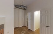This single-floor space is designed with practicality and efficiency in mind. The kitchen serves as a central highlight, featuring a full suite of stainless steel appliances, including a French door refrigerator, an electric range with oven, an over-the-range microwave, and a dishwasher. White upper and lower cabinetry provides ample storage, complemented by dark countertops that offer a clean visual contrast. A single-basin sink with a modern faucet is conveniently positioned along the countertop run. Light ceramic tile flooring covers the kitchen area, adding durability and ease of maintenance to a high-use zone. An exposed ventilation duct runs overhead, adding an industrial touch to the otherwise classic kitchen aesthetic. A six-panel door separates the kitchen from the adjacent areas, contributing to a defined layout. The main living area transitions to neutral-toned carpet, creating a comfortable and cohesive feel throughout. Overhead flush-mount lighting illuminates the space evenly. The overall layout is compact yet well-organized, making efficient use of the available footprint across the single floor.