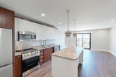 Located at 625 Jackson Ave in New Orleans, this thoughtfully designed one-bedroom, one-bathroom unit offers a contemporary living experience within a compact yet well-utilized floor plan. The open-concept layout seamlessly combines the kitchen, dining, and living areas into a single cohesive space, ideal for both everyday living and entertaining.

The kitchen is a standout feature, showcasing a two-tone cabinetry design with white upper cabinets and rich walnut-toned lower cabinets, complemented by a stainless steel backsplash and a suite of stainless steel appliances including a gas range, microwave, dishwasher, and French door refrigerator. A central island with pendant lighting above provides additional prep space and casual seating. Large sliding glass doors flood the living area with natural light and offer views of the surrounding cityscape.

Rich hardwood-style flooring extends throughout the main living areas and bedroom, adding warmth to the modern aesthetic. The spacious bedroom includes a ceiling fan and direct access to a generous walk-in closet. The bathroom features stone-look tile flooring, a single vanity with wood cabinetry, and a glass-enclosed walk-in shower. Additional conveniences include an in-unit laundry area and hallway storage closet, rounding out this efficiently designed urban residence.