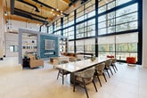 This impressive 2,210 square foot space showcases a striking blend of modern design and industrial elements. The single-floor layout is dominated by soaring floor-to-ceiling windows that flood the interior with natural light and offer expansive views of the surrounding greenery. The open floor plan is characterized by high ceilings with exposed wooden beams and black metal accents, creating a sense of spaciousness and architectural interest.

The main area features a long, white dining table with comfortable seating, perfect for meetings or collaborative work. Adjacent to this is a cozy lounge area with plush sofas and armchairs in muted tones, providing a relaxed setting for casual interactions. The space seamlessly integrates various functional zones, including a sleek kitchenette and multiple seating arrangements that cater to different needs.

Polished concrete floors and a neutral color palette contribute to the space's modern aesthetic, while touches of warmth are added through wooden elements and strategic pops of color in the furnishings. Unique design features, such as the artistic leaf-inspired wall decor and contemporary lighting fixtures, add visual interest and sophistication to the environment.

The versatile layout, coupled with its abundant natural light and thoughtful design, makes this space ideal for a range of purposes, from office use to event hosting, embodying a perfect balance of functionality and aesthetic appeal.