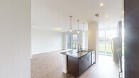 Located at 214 Bellmeade St in Greensboro, NC, this well-appointed 2-bedroom, 2-bathroom residence offers a thoughtfully designed open-concept floor plan across a single level. The combined kitchen and living area serves as the heart of the home, anchored by a sleek kitchen island with dark granite countertops, an undermount double sink, and elegant pendant lighting overhead. The kitchen is equipped with dark cabinetry, a subway tile backsplash, a stainless steel range hood, built-in oven, and a full suite of appliances — all framed by large floor-to-ceiling windows that flood the space with natural light and provide striking views of the adjacent ballpark. The open living room extends from the kitchen and features wood-look flooring and a sliding glass door leading to a private balcony overlooking the stadium. Both bedrooms offer plush carpeting, ceiling fans, and ample room to accommodate a variety of furniture arrangements. The primary bedroom is generously sized and well-lit. Both bathrooms are finished with large-format tile flooring, dark wood vanities, and tiled tub-shower combinations. A dedicated hallway and closet provide practical storage solutions, completing this modern and functional residence.