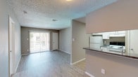 This single-floor 1-bedroom, 1-bathroom unit offers a practical and comfortable layout designed for efficient everyday living. The open-concept living and dining area features light-toned laminate wood flooring, neutral taupe walls, and a textured ceiling, creating a clean and inviting atmosphere. A sliding glass door floods the living space with natural light while providing access to an outdoor area. The kitchen is positioned adjacent to the living space behind a half-wall counter with dark granite-style countertops, offering a functional pass-through feel. White cabinetry, a stainless steel sink, a dishwasher, and a range make up the well-equipped kitchen, which also features matching laminate flooring. The bedroom is a generously sized, carpeted retreat with a ceiling fan and light fixture, a window with outdoor views, and warm neutral tones throughout. The full bathroom includes a tub-shower combination, a white vanity with dark countertop, overhead storage cabinets, a mirror, and light wood flooring. A dedicated laundry or utility closet adds further convenience to the unit. Overall, the space presents a cohesive, functional design with consistent finishes and ample natural light throughout.