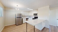 Located at 3719 N Campbell Ave in Tucson, Arizona, this single-floor unit showcases a clean, contemporary design with light wood-style flooring and neutral tones carried consistently throughout. The open-concept living and kitchen area forms the heart of the space, where a ceiling fan with integrated lighting presides over a generous living area bathed in natural light from multiple windows. The kitchen is well-appointed with white shaker cabinetry, a white subway tile backsplash, white quartz countertops, and a full suite of stainless steel appliances including a refrigerator, range, microwave, and dishwasher. A peninsula with a white countertop provides additional prep and casual dining space. The bedrooms are comfortably sized, each featuring light-filled windows, painted cinder block accent walls, and light wood flooring. At least one bedroom includes a built-in closet with rod storage. The bathroom is neatly finished with a white vanity, a tub-shower combination clad in large-format marble-look tile, and coordinating hardware. Throughout the unit, exposed painted cinder block walls lend a distinctive architectural character, complementing the modern updates and creating a bright, functional living environment.