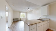 This single-floor unit in Martinez, California (94553) offers a straightforward, functional layout with a clean, neutral aesthetic throughout. The open-concept design connects the kitchen and living area, creating a cohesive and practical living space. Light wood-style flooring runs consistently across the unit, contributing to a bright and unified feel.

The kitchen features white cabinetry, granite-style countertops, a stainless steel sink, and white appliances including a refrigerator and range. A peninsula counter separates the kitchen from the living area, providing additional workspace and a natural division between the two zones. Upper cabinets offer ample storage.

The living area is well-lit by a window overlooking greenery outside, and a ceiling fan with a light fixture is centrally positioned overhead. A wall-mounted HVAC unit provides climate control. The textured ceiling is consistent throughout the space.

A hallway connects the living area to the bedroom and bathroom. The bedroom is a comfortable size with a window framing outdoor views of the surrounding landscape, allowing natural light to fill the room. The bathroom includes a tub and shower combination equipped with accessibility grab bars, a toilet, vanity with granite-style countertop, and wood-style flooring consistent with the rest of the unit.
