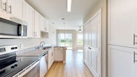 This efficiently designed single-floor unit combines a kitchen and living area in one open, flowing layout, making excellent use of its intimate footprint. The kitchen is well-appointed with white shaker-style cabinetry, granite countertops, and a full suite of stainless steel appliances including a refrigerator, electric range, over-the-range microwave, and dishwasher. A peninsula counter with pendant lighting above serves as a natural divider between the kitchen and living space, while also providing additional prep and seating area. Light hardwood flooring runs continuously throughout the unit, enhancing the sense of openness and cohesion. The living area is bright and airy, benefiting from large windows and a sliding glass door that opens to a private balcony, offering pleasant outdoor views and an abundance of natural light. A ceiling fan with integrated lighting provides both comfort and ambiance in the living space. The bathroom is clean and functional, featuring a full soaking tub with a surround enclosure and brushed nickel fixtures. Neutral warm-toned walls throughout complement the light flooring, creating a fresh, modern aesthetic. The unit also includes a utility panel conveniently located near the entryway.