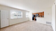 This 2-bedroom, 1-bathroom unit in Baltimore, MD is thoughtfully laid out across a single floor, offering a comfortable and practical living space. The carpeted living room is bright and open, featuring large windows that allow natural light to fill the room, creating a welcoming atmosphere. It connects seamlessly to the kitchen, which is outfitted with warm honey-toned cabinetry, a stone-look backsplash, granite-style countertops, and a full suite of black appliances including a refrigerator, range, and over-the-range microwave. Light tile flooring and a pass-through counter enhance the kitchen's functionality. The primary bedroom is generously sized, offering two windows that frame views of surrounding greenery, a ceiling fan with light fixture, and a closet. The second bedroom also features a ceiling fan, natural light from a window, and plush carpeting. A notable feature of the primary bedroom is the multiple built-in closet doors, providing ample storage. Neutral walls and wall-to-wall carpet throughout the living spaces contribute to a cohesive and clean aesthetic. A hallway and staircase complete the layout, providing easy circulation throughout the unit.