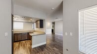 This single-story, 2-bedroom residence offers a comfortable and functional layout across a generously sized floor plan. The open-concept living room serves as the heart of the home, featuring dark hardwood-style flooring, neutral gray walls, and a striking tile-surround fireplace flanked by a decorative arched alcove. A sliding glass door floods the space with natural light and provides outdoor access. The kitchen is well-equipped with dark wood cabinetry, light quartz countertops, a peninsula with a breakfast bar, recessed lighting, and a stainless steel sink — all set atop warm wood-look flooring. An arched pass-through connects the kitchen to the living area, reinforcing the open flow of the space. Both bedrooms are carpeted and bright, with horizontal blinds on the windows. The spacious primary bedroom includes mirrored sliding closet doors. A dedicated closet provides additional storage throughout the home. The laundry room is a standout functional feature, offering full-size washer and dryer units, dark wood overhead cabinetry, and a quartz folding counter. Throughout the home, clean white baseboards and a consistent neutral palette create a cohesive, modern aesthetic.