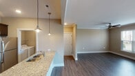 Located at 18300 Wheeler Rd in Westfield, Indiana, this single-floor residence offers a well-designed, open-concept layout that seamlessly connects the main living areas. The kitchen is a standout feature, showcasing rich dark-wood cabinetry, granite countertops, a subway tile backsplash, and a full suite of stainless steel appliances including an electric range, over-the-range microwave, and refrigerator. A peninsula with a stainless steel sink and pendant lighting creates an inviting bar-style seating area that opens directly to the living space. A convenient in-unit laundry area is accessible from the kitchen.

The living room is generously proportioned, with dark hardwood-style flooring, crown molding, and a ceiling fan. Large sliding glass doors flood the room with natural light and provide access to an outdoor area with exterior views. A built-in bench with beadboard detailing adds a charming architectural touch near the entryway.

The bedroom features plush carpet, a large window with blinds overlooking the outdoors, and ample natural light. The bathroom is well-appointed with a dark-wood vanity, granite countertop, a wide mirror, and a full tub-shower combination. Neutral warm-toned walls and consistent flooring throughout tie the entire space together in a cohesive, modern aesthetic.