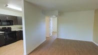 This interior space showcases a modern, minimalist design with an emphasis on openness and flow. The room features smooth, off-white walls that create a clean, bright atmosphere. The flooring is a standout element, boasting warm-toned hardwood planks that run throughout the visible area, adding a touch of natural elegance to the space.

The layout appears to be open concept, with no visible partitions in the main area. This design choice promotes a sense of spaciousness and allows for versatile use of the space. A notable architectural feature is the doorway visible in the center of the image, which leads to an adjoining room, hinting at a well-connected floor plan.

The ceiling appears to be standard height with a smooth, white finish that complements the walls. While no windows are visible in this particular view, the space is well-lit, suggesting potential natural light sources in other areas of the home.

Overall, this interior presents a blank canvas, ready for personalization. Its neutral color palette and open design make it adaptable to various décor styles and functional needs, whether for residential or commercial use.