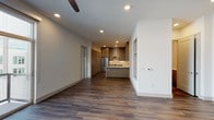 This single-floor residence is designed with a clean, contemporary aesthetic that prioritizes open living and functional design. The main living area is generously proportioned, featuring wood-look plank flooring, recessed lighting, and a ceiling fan. Large sliding glass doors connect the living space to a private balcony, filling the interior with natural light and providing outdoor views of the surrounding urban environment.

The kitchen is a standout feature, equipped with warm-toned shaker-style cabinetry extending to the ceiling for ample storage, white quartz countertops, a subway tile backsplash, and a full suite of stainless steel appliances including a double oven range, refrigerator, and dishwasher. A wall-mounted range hood anchors the cooking area, while a peninsula with a waterfall-edge counter defines the boundary between the kitchen and living space.

The bedroom is carpeted for comfort and features two windows with roller shades that frame exterior views. Ceiling fans are present throughout for added climate control.

Two bathrooms serve the unit. The primary bathroom offers a dual-sink vanity with taupe cabinetry, open shelving, a glass-enclosed tub-shower combination, and wood-look tile flooring. The secondary bathroom is compact and efficiently laid out with a vanity and toilet.