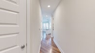 This single-floor residence is thoughtfully designed with a clean, contemporary aesthetic that flows seamlessly from room to room. The interior is anchored by rich hardwood flooring that runs through the main living and kitchen areas, complemented by crisp white walls and bright recessed lighting throughout.

The kitchen serves as a central highlight, featuring a large island with a gray quartz-style countertop, white shaker cabinetry extending to the ceiling, a marble-style tile backsplash, and a full suite of stainless steel appliances including a range, microwave, and refrigerator. A striking cluster of pendant lights hangs above the island, adding a modern, decorative touch. The kitchen opens directly to a spacious living area bathed in natural light from a wall of large windows offering outdoor views.

A well-proportioned hallway connects the living spaces to the private rooms, with recessed lighting guiding the way. The bedrooms feature soft, neutral carpeting and panel-style doors, providing a comfortable, quiet retreat. One bedroom connects directly to an adjacent room, adding flexibility to the layout.

The bathroom is finished with hardwood-style flooring, white cabinetry with a gray countertop, and a tiled shower-tub combination with a curved rod, delivering a clean and functional design.