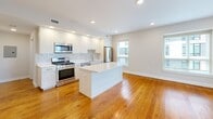 This two-bedroom, two-bathroom residence in Boston, MA offers a well-designed single-level floor plan that maximizes functionality within a compact footprint. The open-concept kitchen and living area serves as the heart of the home, featuring warm hardwood floors that extend throughout the space. The kitchen is outfitted with white shaker-style cabinetry, a subway tile backsplash, stainless steel appliances including a gas range, microwave, dishwasher, and refrigerator, as well as a central island with a light wood finish and quartz countertop that provides additional workspace and casual seating.

Both bedrooms are comfortably sized, finished with the same rich hardwood flooring and neutral wall tones. Large windows fitted with blinds allow natural light to filter in while offering views of the surrounding neighborhood. Each bedroom includes dedicated closet space for practical storage.

The two bathrooms reflect a clean, modern aesthetic. One features large-format light stone tile flooring, a window for natural light, and grab bar accessibility features. The second bathroom offers a wall-mounted floating vanity with a vessel sink, an oversized mirror, and tile flooring. The residence includes two closets throughout, contributing to overall storage efficiency. The consistent use of neutral tones and quality finishes creates a cohesive, move-in-ready atmosphere.