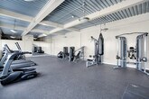 Located at 650 S Spring St in the heart of Downtown Los Angeles, this fitness center offers a well-equipped, single-floor workout space designed to accommodate a variety of exercise needs. The room features a durable rubber speckle flooring throughout, providing a safe and functional surface for all types of training.

The space is outfitted with a comprehensive selection of TRUE-brand cardio machines, including treadmills, ellipticals, and stationary bikes, all arranged to maximize floor space and ease of movement. A dedicated strength training zone features a multi-use cable machine, a punching bag, and a selection of free weights and exercise balls. A padded stretching and floor exercise area is clearly defined along one wall, providing a dedicated zone for mat-based workouts.

A full-length mirror spans one wall, enhancing the sense of space and allowing users to monitor their form. Pendant globe lights hang from an exposed corrugated metal ceiling with structural beams, lending the space an industrial-modern aesthetic. Natural light filters in through multiple windows, one of which frames a direct view of the Downtown Los Angeles skyline, adding a distinctive urban backdrop to every workout session.