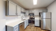 This single-story residence in Louisville, Kentucky, presents a well-organized layout with a neutral color palette of soft grays and warm tones throughout. The kitchen serves as a functional centerpiece, outfitted with gray shaker-style cabinetry, white countertops, and a full suite of stainless steel appliances including a range, over-the-range microwave, dishwasher, and refrigerator. Wood-look flooring runs through the kitchen, adding warmth and durability to the space.

The open transition between the kitchen and living areas is defined by a partial wall, creating a natural flow while maintaining distinct zones. The living area features wood-look flooring at the entry, transitioning to plush carpeting that extends through the bedrooms. Each bedroom is equipped with a ceiling fan and light fixture, and benefits from natural light through blinded windows. The primary bedroom stands out with dual closets, offering generous storage. Additional bedrooms are comparably sized, each with their own window and ceiling fan.

The bathrooms include one full bath with a tub-shower combo, wood-look tile flooring, a gray vanity with white countertop, and ample storage. A second bathroom features a walk-in shower. Together, these spaces deliver a clean, functional, and cohesive living environment.
