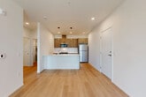 Located in Marysville, WA, this well-designed one-bedroom, one-bathroom unit offers a thoughtful open-concept layout that seamlessly connects the living room, dining area, and kitchen into a single cohesive space. Light hardwood-style flooring runs throughout the main living areas, complementing the clean white walls and recessed lighting that give the unit a bright, contemporary feel.

The kitchen is a standout feature, equipped with warm wood-tone cabinetry, white subway tile backsplash, stainless steel appliances including a refrigerator, range, and microwave, and a peninsula with a white quartz countertop and built-in sink. Stylish pendant lights hang above the peninsula, adding a modern design touch. A hallway leads to the private bedroom, which is finished with plush carpet flooring and a window offering outdoor views, bringing in natural light. Two closets provide ample storage throughout the unit.

The bathroom features a full tub-shower combination, wood-tone vanity with a white countertop, and light hardwood-style flooring. Additional highlights include a private balcony, an in-unit laundry area, and a wall-mounted mini-split system for climate control. The overall ambiance is clean, modern, and move-in ready.