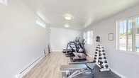 Located at 126 W Ahwanee Ave in Sunnyvale, CA, this dedicated exercise room offers a thoughtfully organized fitness space designed to support a full range of workout routines. The room features light gray walls, smooth ceilings with flush-mount lighting fixtures, and light-toned laminate wood flooring that gives the space a clean, modern feel. Protective rubber flooring mats are strategically placed beneath the equipment zones.

Natural light streams in through multiple horizontal windows positioned along the upper portion of the walls, keeping the space bright and airy throughout the day. A glass-paneled door provides direct access to an outdoor area, further enhancing ventilation and openness.

The exercise room is equipped with a cable functional trainer paired with an adjustable workout bench, ideal for strength training. A dumbbell rack stocked with a range of free weights sits nearby for versatile resistance training. Cardio equipment, including an elliptical trainer and a treadmill, occupies one section of the room, providing effective aerobic workout options. Additional accessories such as a stability ball, resistance mats, and a foam roller round out the facility.

Informational fitness posters are displayed on the walls, adding a practical, educational touch to the environment. A baseboard heating unit ensures comfort during cooler months. Overall, this exercise room delivers a compact yet fully functional fitness environment suited for personal or small-group use.