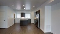 This 3-floor space showcases a contemporary design with a clean, modern aesthetic throughout. The kitchen serves as a standout feature, equipped with stainless steel appliances including a French door refrigerator and a gas range. Dark charcoal cabinetry provides a striking contrast against the white countertops and light-toned walls, creating a sophisticated, two-toned palette. A central island offers additional workspace and visual definition within the open layout.

Recessed lighting is embedded throughout the ceiling, providing consistent, even illumination across the space. The flooring consists of dark hardwood-style planks that run continuously, lending warmth and cohesion to the interior. Multiple windows fitted with white horizontal blinds allow natural light to filter in, brightening the kitchen area.

White baseboards and trim provide crisp finishing details against the neutral gray walls. The layout appears open and functional, with clear sightlines across the main level. Spanning three floors, this space offers substantial vertical living potential, with the main level setting a polished, practical tone for the rest of the home.