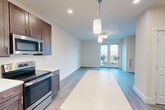 This well-designed one-bedroom, one-bathroom residence in South Burlington, Vermont offers a thoughtfully planned layout across a single floor. The open-concept living, dining, and kitchen area serves as the heart of the home, featuring light hardwood-style flooring that flows seamlessly throughout. The kitchen is outfitted with rich dark-brown cabinetry, white quartz countertops, a stainless steel appliance suite including a refrigerator, electric range, microwave, and dishwasher, and a central island with pendant lighting overhead — ideal for both meal preparation and casual dining. French doors in the living area open to a private balcony, filling the space with natural light and outdoor views. The bedroom is a comfortable, well-proportioned retreat with a large window overlooking the balcony, continuing the warm hardwood-style flooring and neutral wall tones. The bathroom features a wide vanity with dark cabinetry, a generous mirror, and a tall storage tower for added organization. Additional highlights include three closets providing ample storage, a dedicated laundry area, and a hallway connecting all spaces efficiently. The clean, contemporary finishes and modern design make this a polished and functional residence.