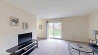 Located at 5996 Wonderland Pl in Portage, Indiana, this single-floor, one-bedroom, one-bathroom unit offers a thoughtfully arranged layout across a comfortable footprint. The living room serves as the heart of the home, featuring plush carpeting, neutral warm-toned walls, and a large sliding glass door that floods the space with natural light and opens to a view of a lush green lawn. The open feel of the living area is enhanced by its clean sightlines connecting to the hallway and adjacent rooms. The kitchen is equipped with dark wood cabinetry, tile-style flooring, black appliances including a full-size refrigerator and dishwasher, a double-basin sink, and a convenient louvered-door pantry closet. The bedroom is generously proportioned with soft carpeting, a large window offering natural light and outdoor views, and ample wall space. A dedicated office provides a quiet, carpeted workspace with its own window, making it ideal for remote work or study. The full bathroom features a tub-shower combination, a dark wood vanity with a white countertop, and tile flooring. A connecting hallway ties all rooms together efficiently, completing this well-organized and functional single-level home.