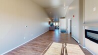 Located at 1265 Lear Ln in Hobart, Wisconsin, this 2-bedroom, 2-bathroom home offers a thoughtfully designed single-floor layout with stylish, modern finishes throughout. The open-concept living and kitchen area is immediately impressive, featuring soaring vaulted ceilings that amplify the sense of space and allow natural light to pour in through large sliding glass doors that lead to an outdoor balcony with neighborhood views. A sleek built-in fireplace serves as a focal point in the living area, complemented by durable wood-look flooring underfoot. The kitchen is well-appointed with rich dark cabinetry, stone-look countertops, black appliances including a dishwasher and refrigerator, and a trio of windows above the sink that flood the space with natural light. Both bathrooms mirror the kitchen's design aesthetic, featuring dark vanities with stone countertops and framed mirrors. The generously sized primary bedroom features plush carpeting, a ceiling fan, vaulted ceilings, and direct access to its own private bathroom with a dedicated closet. The second bedroom also offers carpet flooring, a wall unit, and a bright window. Additional highlights include multiple closets, a dedicated laundry area, and a hallway connecting all rooms seamlessly.