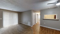 This single-floor residential unit offers a practical and straightforward layout designed for comfortable everyday living. The main living area is finished with wall-to-wall carpet and painted in a neutral gray-blue palette, creating a calm and cohesive atmosphere throughout. Vertical blinds dress a sliding glass door that opens to an outdoor area, allowing natural light to filter into the space. A pass-through window connects the living area to the kitchen, enhancing the sense of openness between the two spaces.

The kitchen features hardwood-style flooring and includes a stainless steel refrigerator, providing a clean and functional workspace. Adjacent to the kitchen is a dedicated laundry area equipped with washer hookups and wire shelving overhead for additional storage.

The bedrooms continue the carpeted flooring and neutral wall tones. One bedroom benefits from dual windows that invite generous natural light, while another features a sliding glass door with vertical blinds, offering direct outdoor access. Closet space is available within the bedrooms to support storage needs.

The bathroom is outfitted with a full-size soaking tub and shower combination featuring clean white surrounds and chrome fixtures. Textured ceilings are consistent throughout the unit, and white baseboards provide a crisp finish to each room.