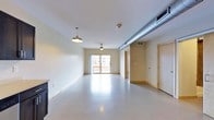 This single-floor space offers a clean, open layout with an industrial-modern aesthetic. The interior is defined by smooth, polished concrete flooring that reflects natural light throughout the room, contributing to a bright and airy atmosphere. Neutral-toned walls provide a versatile backdrop, while the white ceiling showcases an exposed metal duct that runs the length of the space, adding an industrial character.

Lighting is thoughtfully integrated, with a pendant barn-style fixture and a ceiling fan with a built-in light, ensuring both style and functionality. A large sliding glass door at the far end of the main area allows generous amounts of natural light to pour in and offers views of the surrounding urban environment, creating a strong connection between the interior and the outdoors.

The layout is notably open and flexible, making it well-suited for a variety of uses. Along the perimeter, light wood-trimmed doorways lead to additional rooms or utility areas, providing practical organization without interrupting the openness of the main floor. HVAC vents are integrated into the ceiling, ensuring climate comfort throughout. Overall, the space combines raw, utilitarian elements with clean finishes to create a functional and adaptable environment.